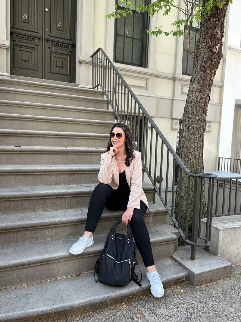 Kelly the GRATI shop founder, sitting on steps in NYC wearing a Lay & V bodysuit, tan blazer with a travel backpack